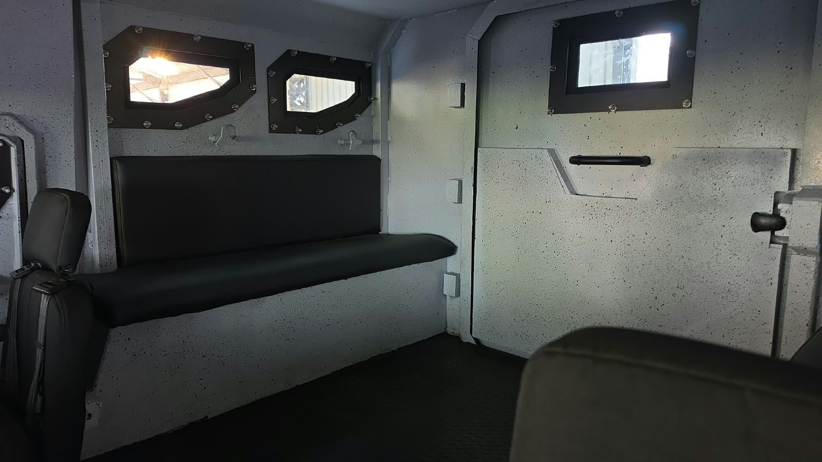 Interior de un vehículo blindado con una banca tapizada y ventanas blindadas montadas en paneles de acero